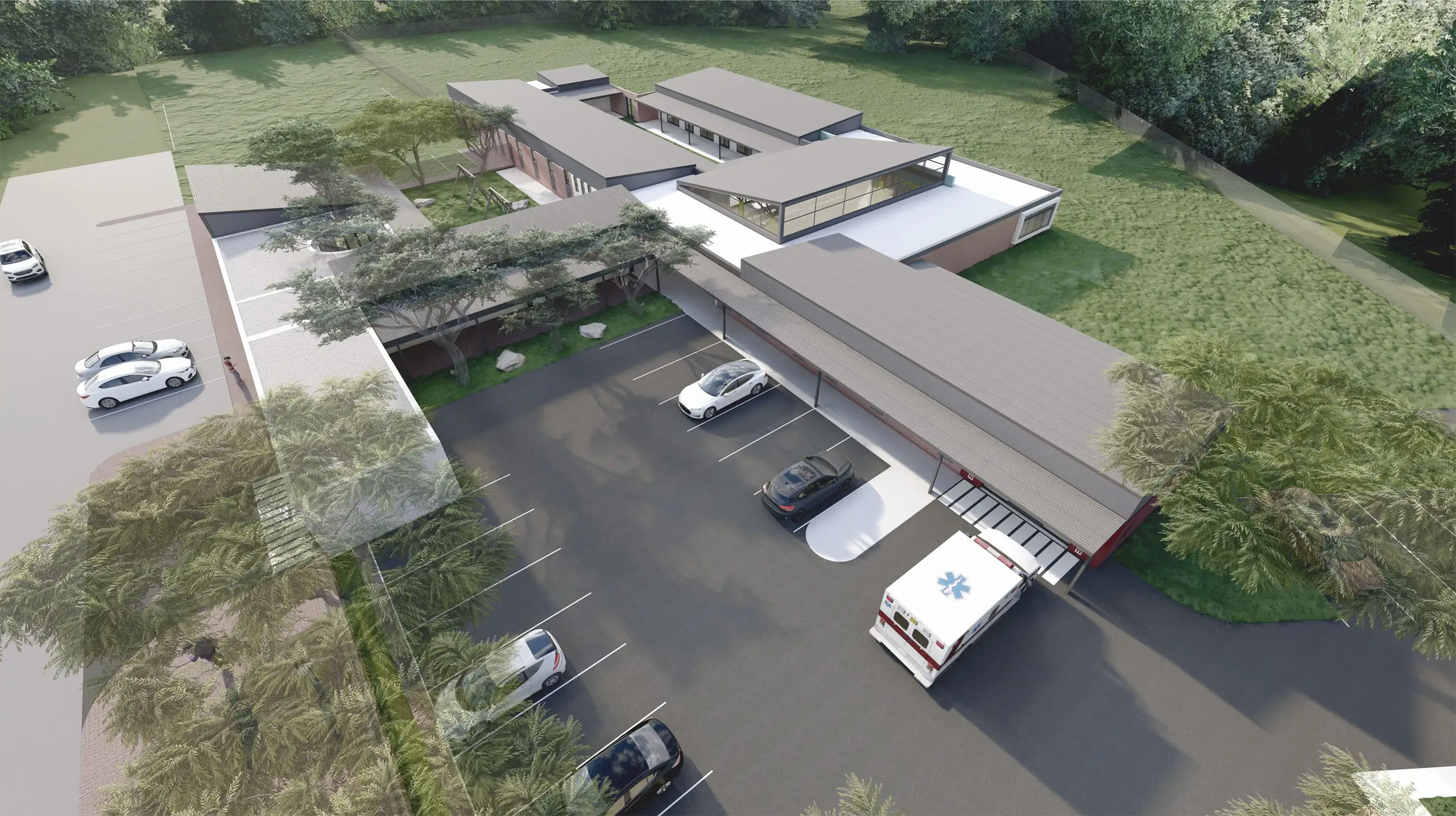 Aerial view of a modern single-story commercial or medical facility with a flat grey roof, ample parking, and surrounding green areas, showing a clean architectural design