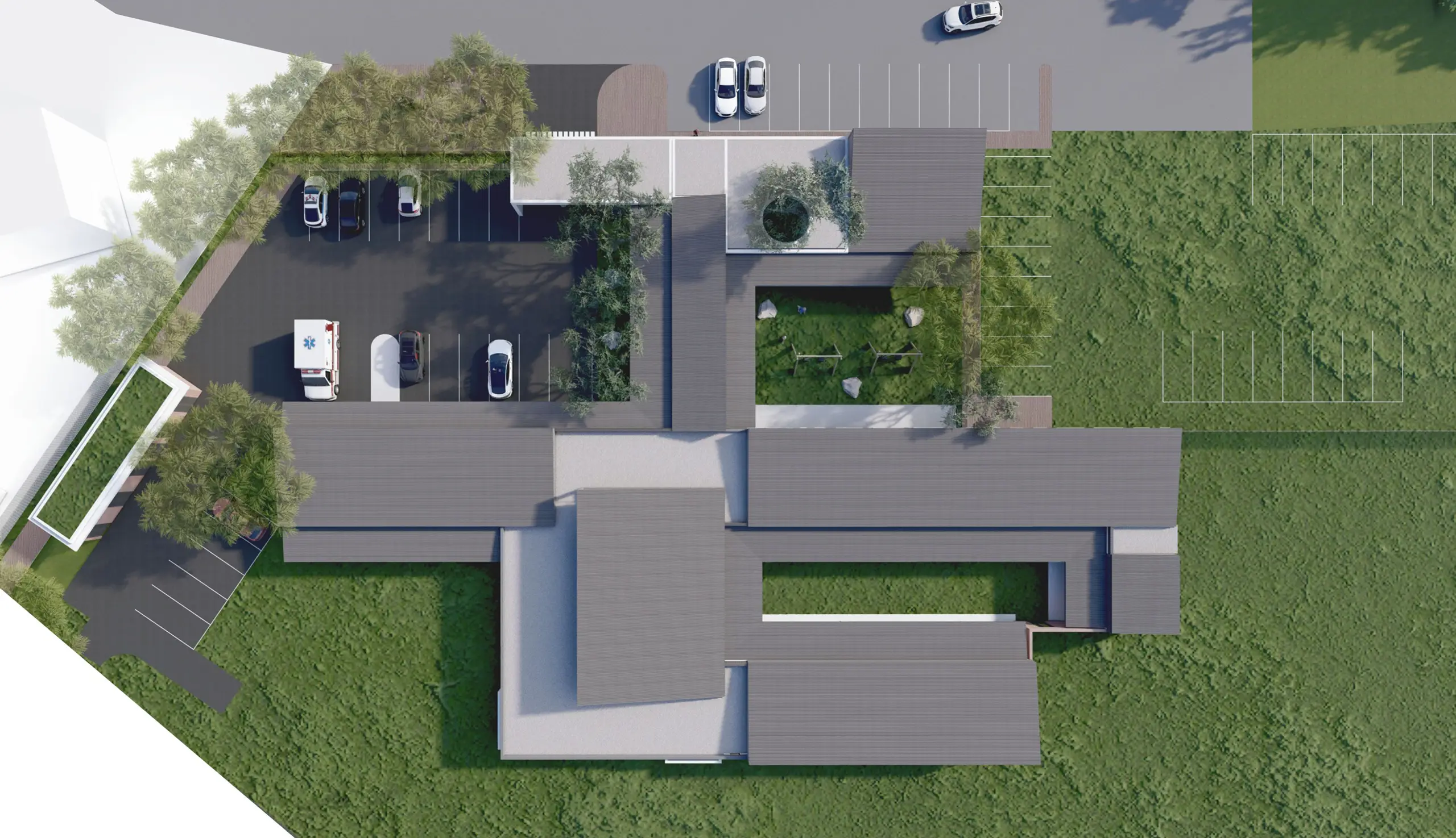 Top-down site plan view of a building complex with a central courtyard or open space, showing the roof layout, parking areas, and surrounding green landscape